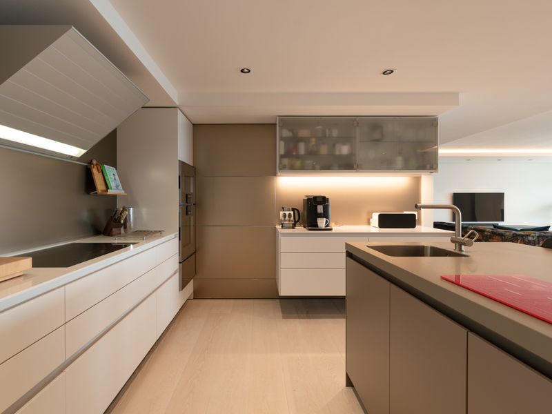 Modern open-plan kitchen featuring sleek cabinetry, integrated appliances, a central island with a sink, and recessed lighting.