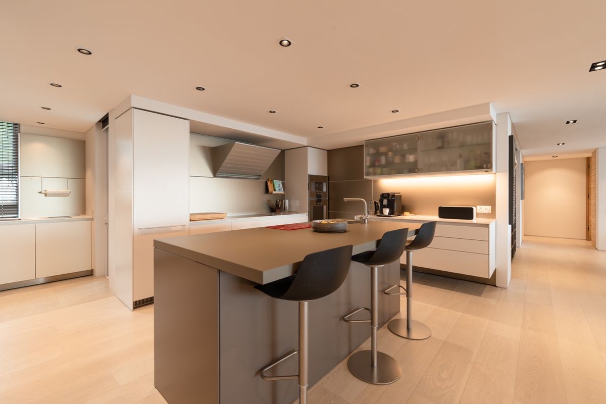 Modern open-plan kitchen featuring a central island with breakfast bar, integrated cabinetry, built-in oven, extractor fan, and recessed ceiling lighting.