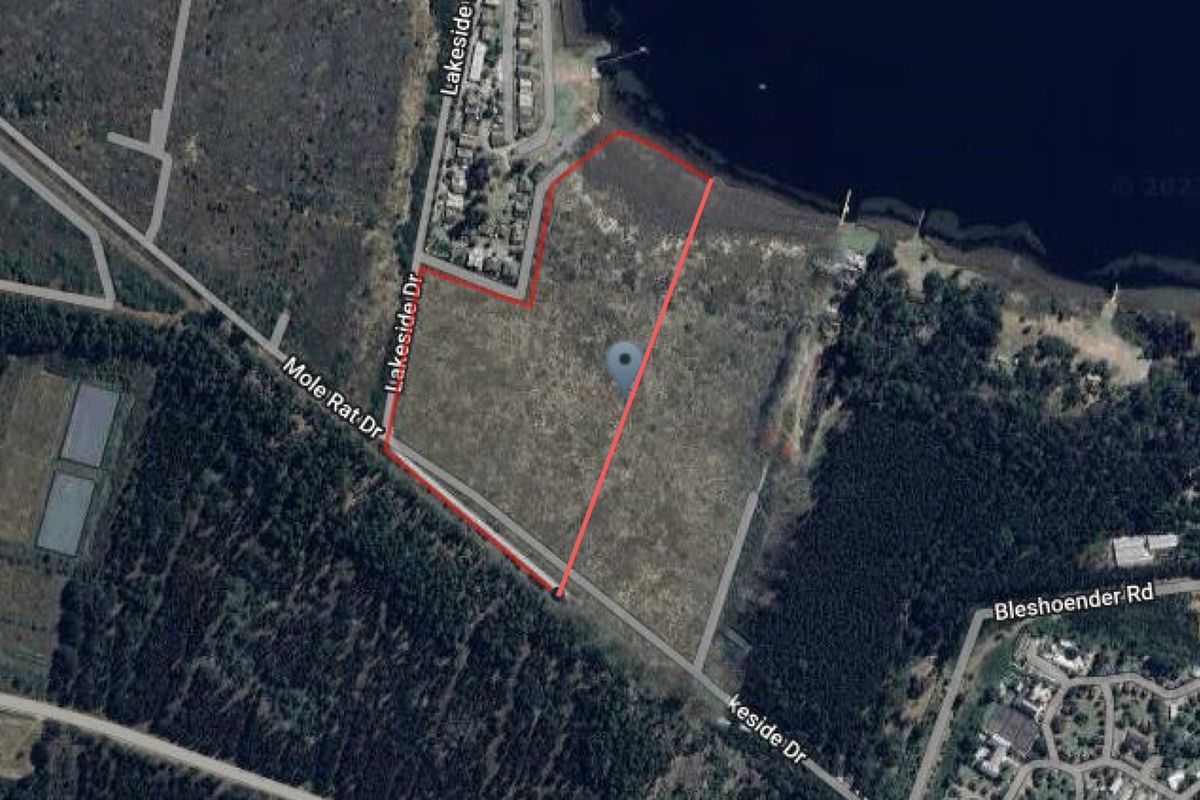 Aerial view of a vacant residential land parcel outlined in red, situated near a lake and local road infrastructure.