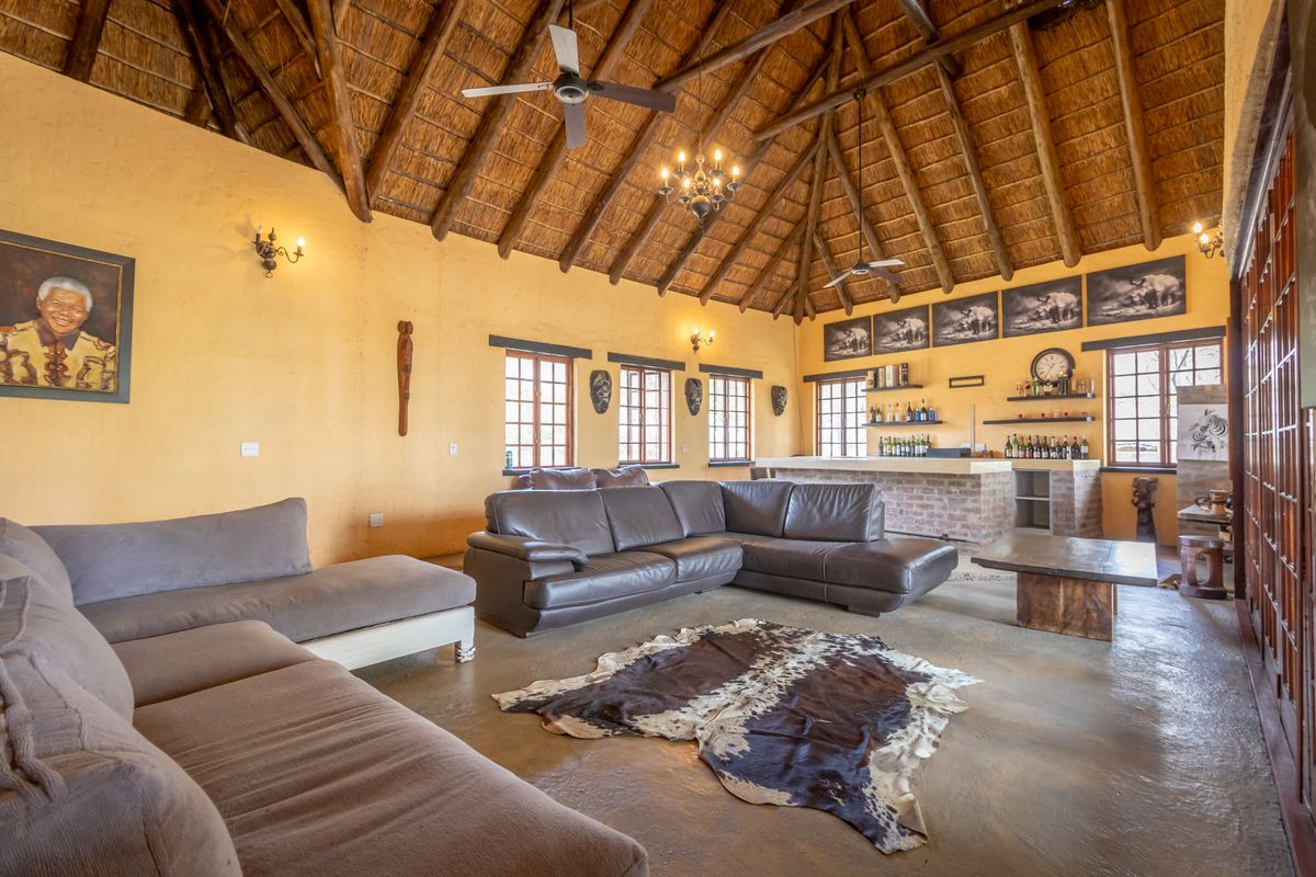 Spacious living area featuring a high vaulted thatched roof, exposed timber beams, built-in brick bar, and polished concrete flooring.
