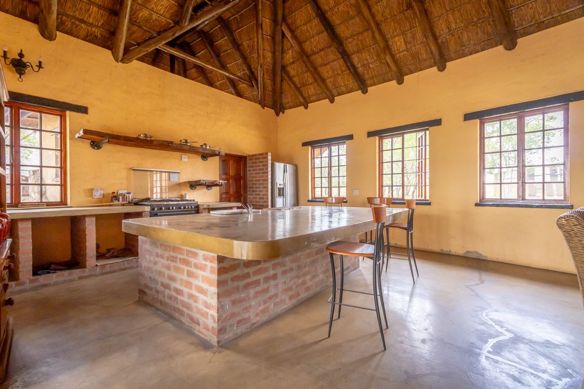 Rustic farmhouse kitchen featuring a large brick-based island, exposed timber thatch ceiling, and built-in concrete countertops with a gas stove.