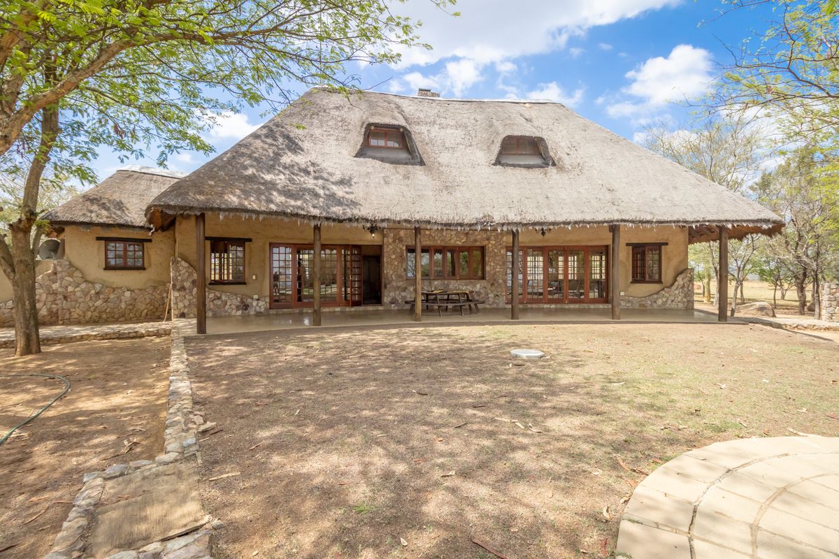 Rear view of a traditional thatched-roof farmhouse featuring stone cladding, timber-framed doors, and a spacious covered patio area overlooking the garden.