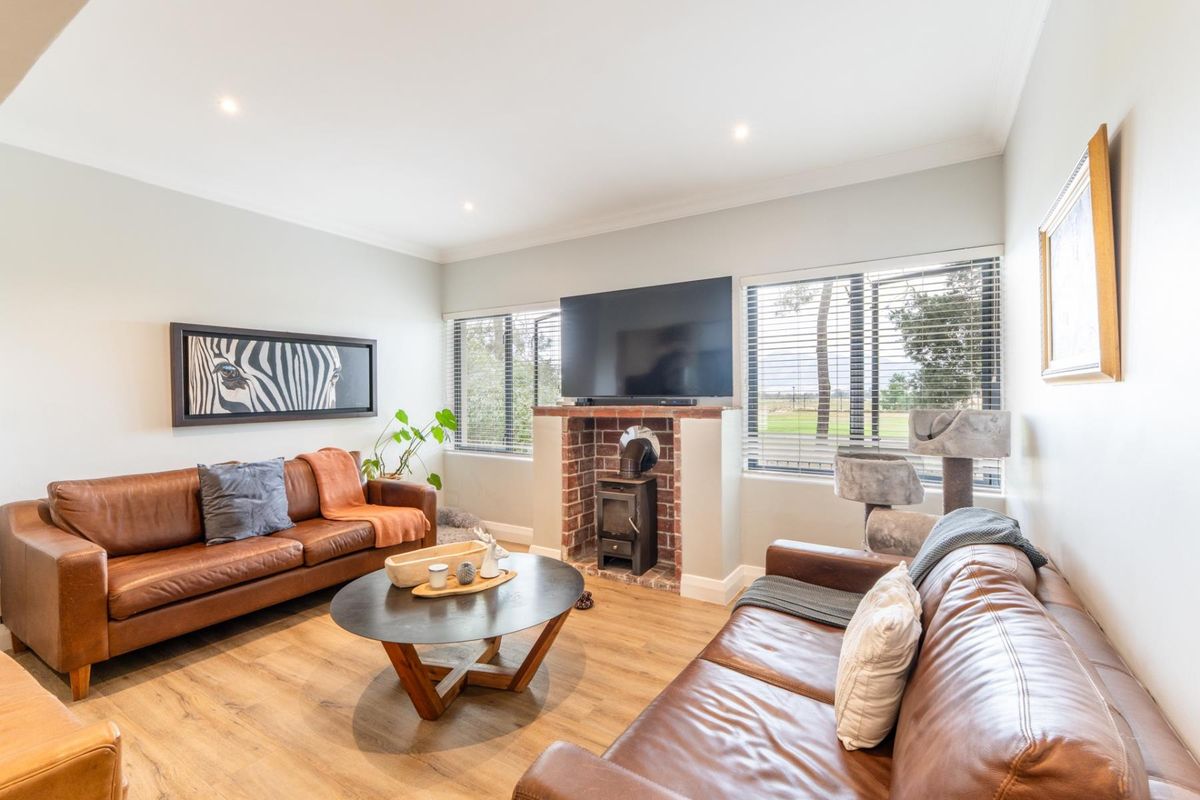 A comfortable living room featuring a brick fireplace with a wood-burning stove, wood-look flooring, and large windows providing natural light.