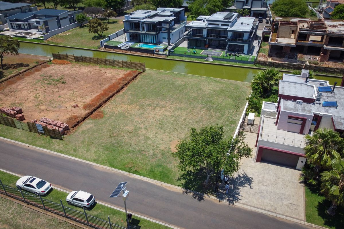 An aerial view of a vacant residential plot situated in a developed estate, featuring level grassed land and proximity to a canal.