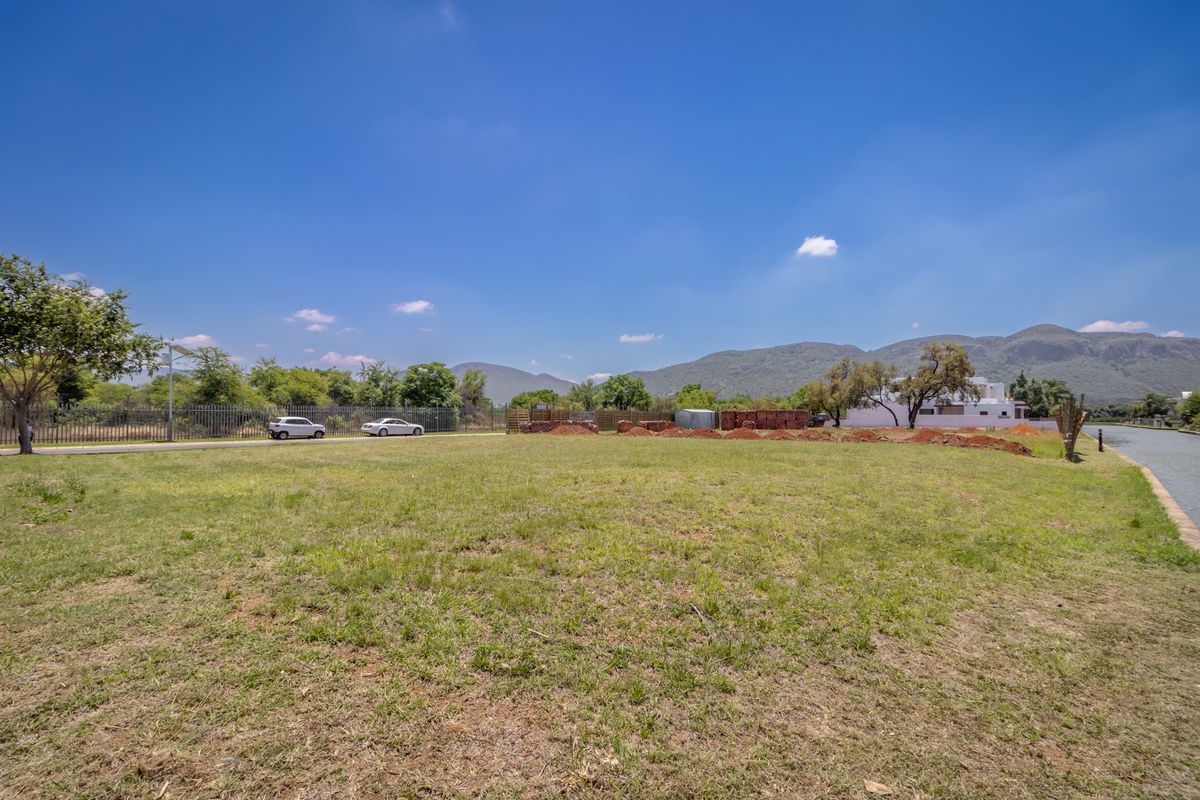 A vacant residential plot of land featuring open grass, perimeter fencing, and scenic mountain views, situated adjacent to a canal.