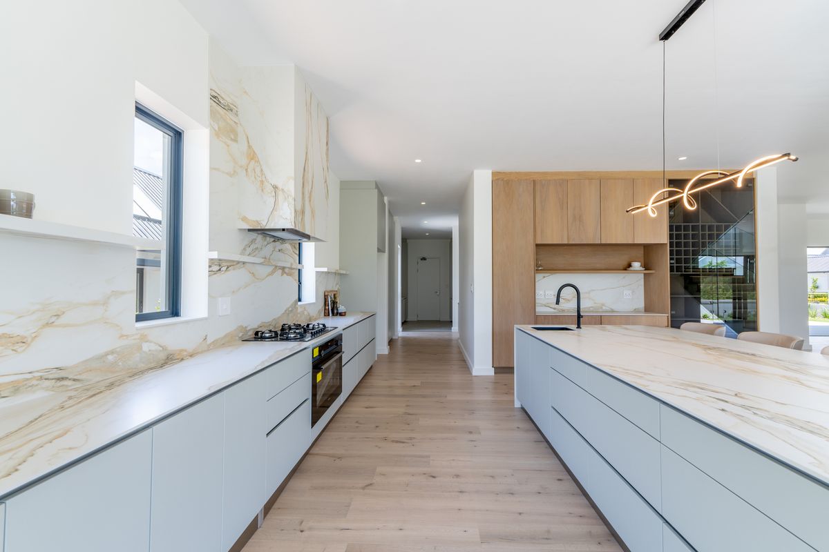 Modern kitchen featuring marble-look stone splashbacks, integrated cabinetry, a central island with a sink, and high-end built-in appliances.