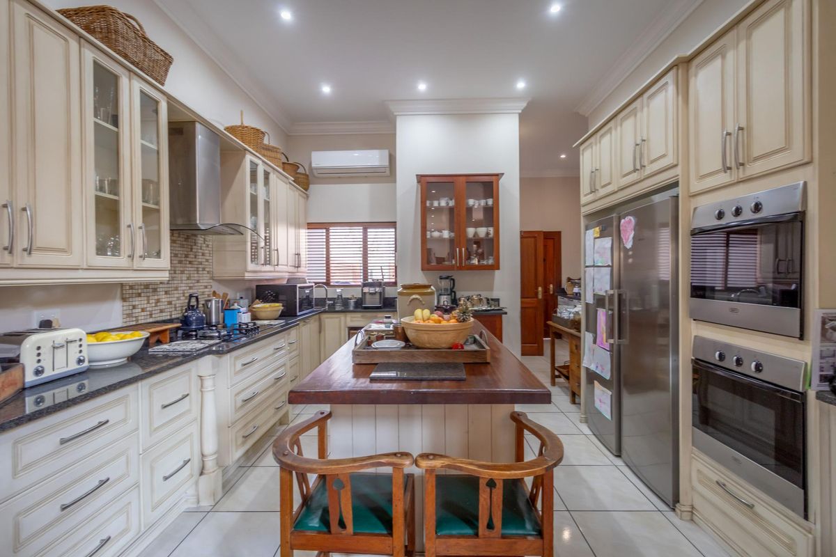 A well-appointed kitchen featuring classic cabinetry, a central timber-topped island, granite countertops, and integrated stainless steel appliances including a double oven.