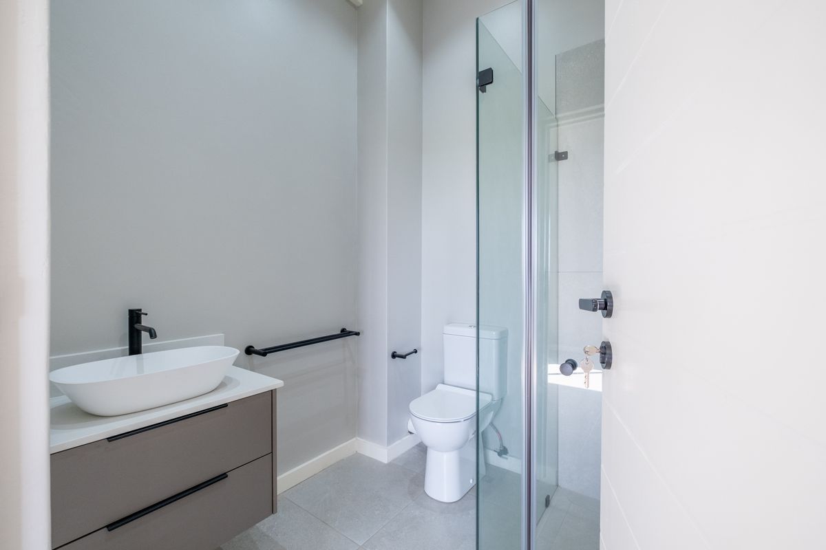 Modern bathroom featuring a floating vanity with a vessel sink, matte black fixtures, a glass-enclosed shower, and neutral floor tiling.