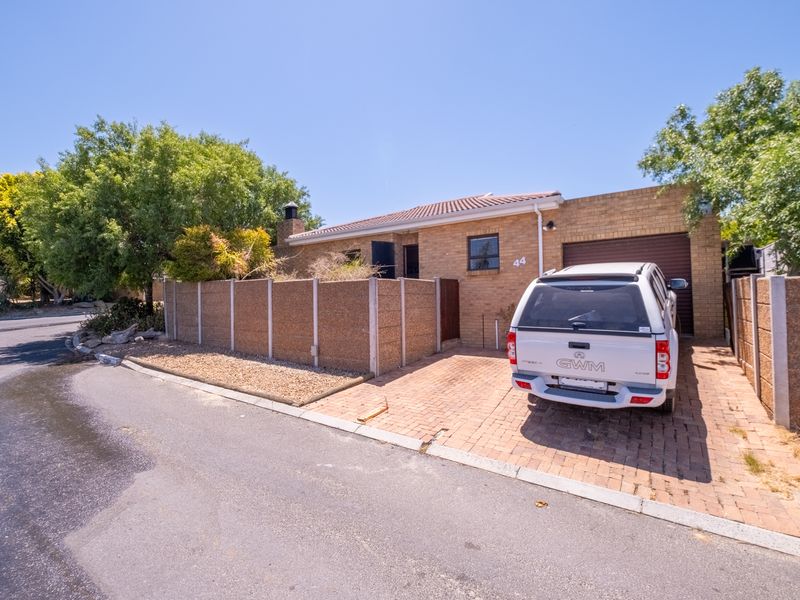 Front exterior view of a brick townhouse featuring a paved driveway, single garage, and precast concrete boundary wall.
