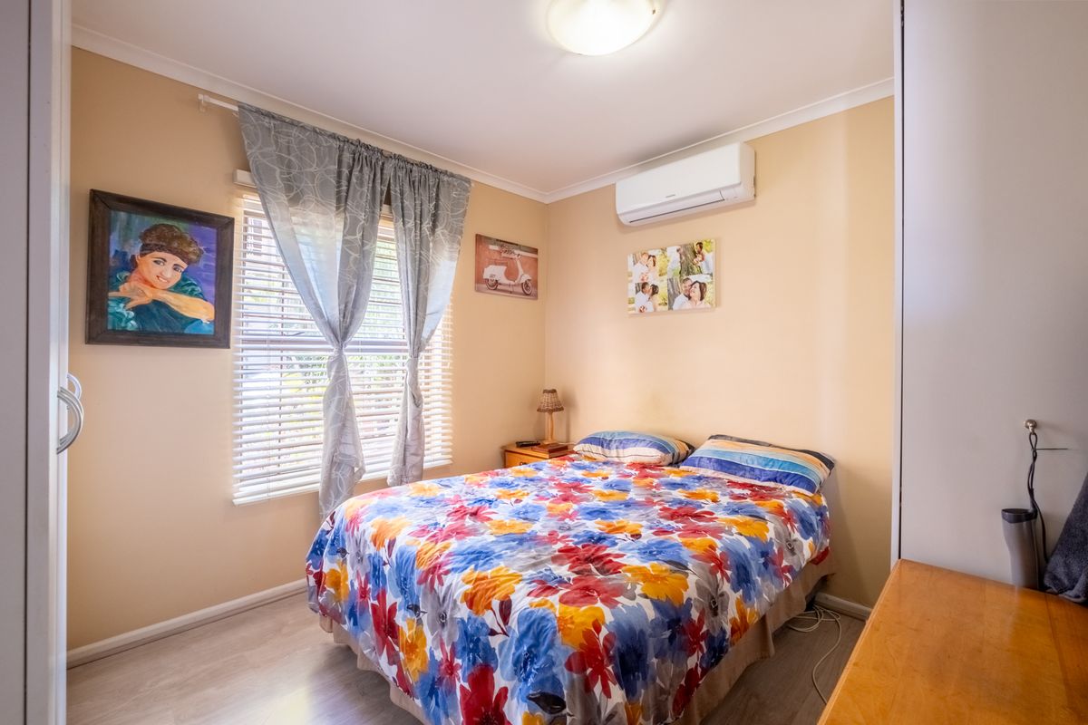 A functional bedroom featuring light-toned flooring, a wall-mounted split-system air conditioner, and a built-in wardrobe.