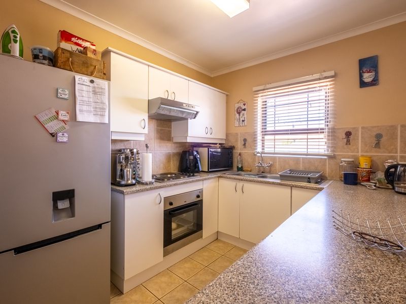 A functional kitchen featuring white cabinetry, laminate countertops, tiled backsplash, and integrated appliances including an oven and extractor fan.