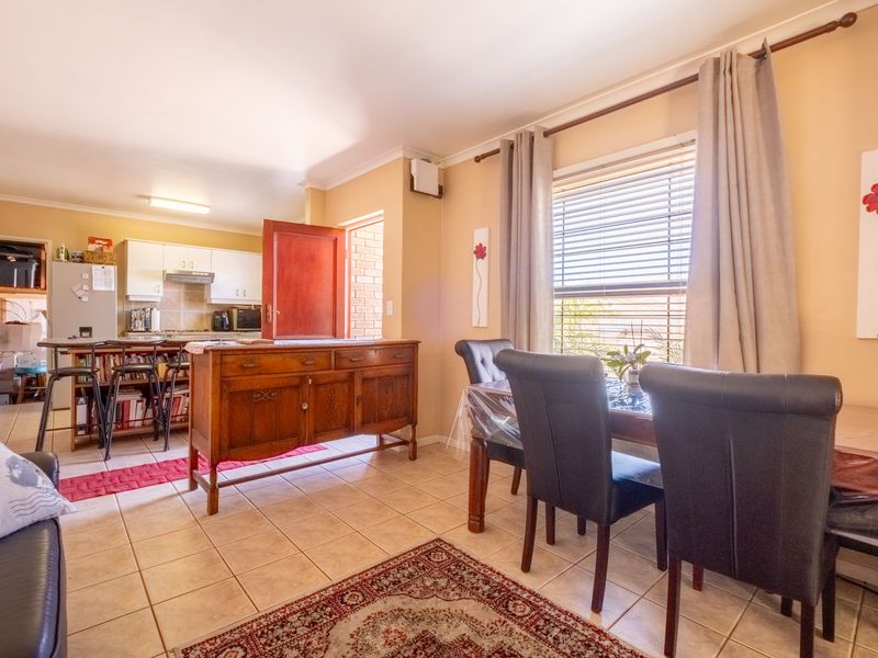 Open-plan living and dining area featuring tiled flooring and an adjoining kitchen with built-in cabinetry and appliances.