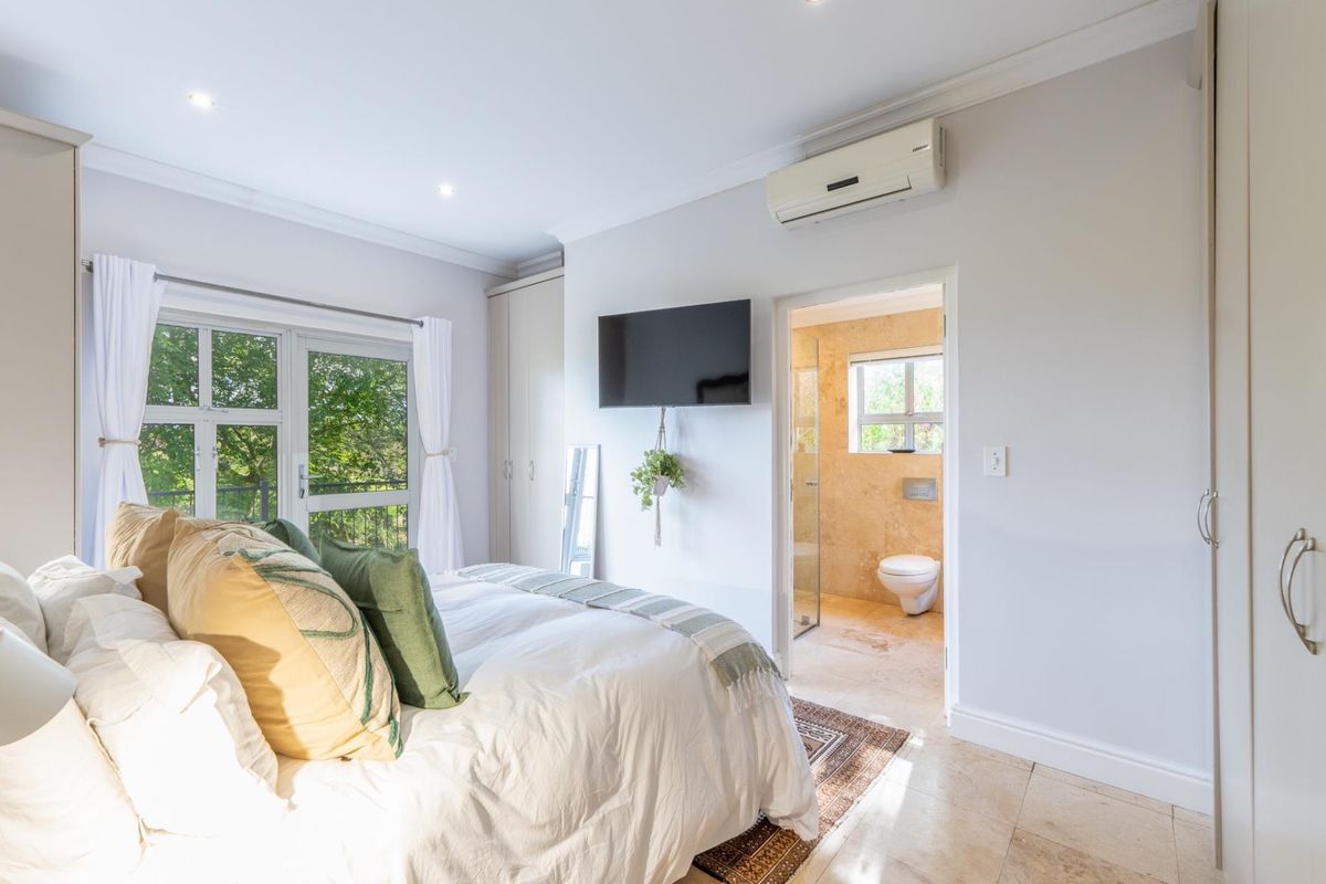 A bright bedroom featuring built-in cupboards, a wall-mounted air conditioning unit, and an en-suite bathroom with stone-tiled finishes.