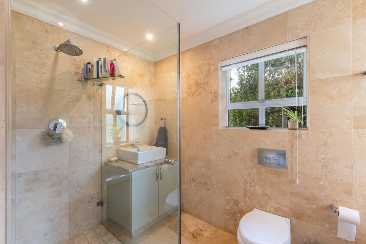 Modern bathroom featuring floor-to-ceiling travertine tiling, a glass-enclosed walk-in shower, a vessel sink vanity, and a wall-mounted toilet.