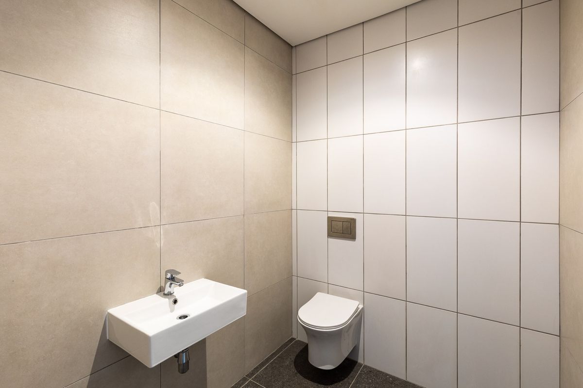 A modern, minimalist bathroom featuring a wall-mounted basin and a concealed cistern toilet with neutral floor-to-ceiling tiling.