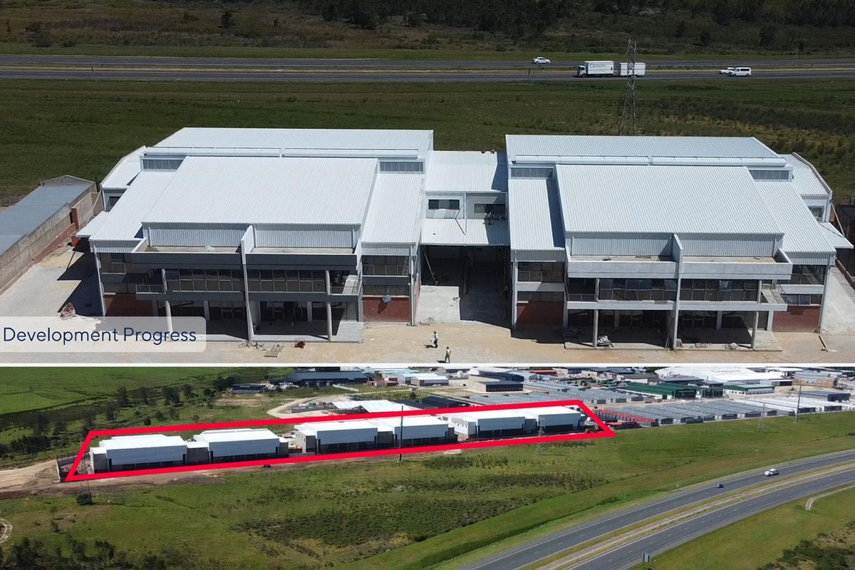 Aerial view of a commercial retail development under construction, featuring large warehouse-style structures with metal roofing and expansive parking areas.