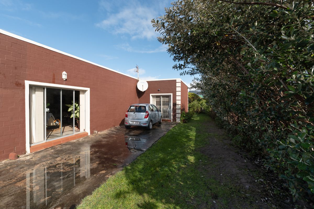 Rear exterior view of the property featuring a paved driveway, sliding glass doors, and a side garden area with mature trees.