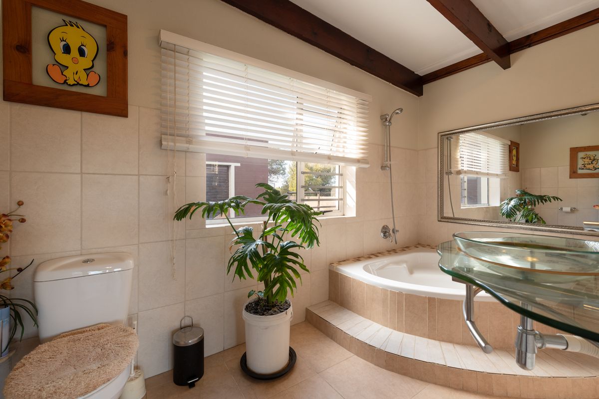 A bathroom featuring a built-in corner bathtub, tiled surround, wall-mounted shower head, and a glass vessel sink with a chrome faucet.