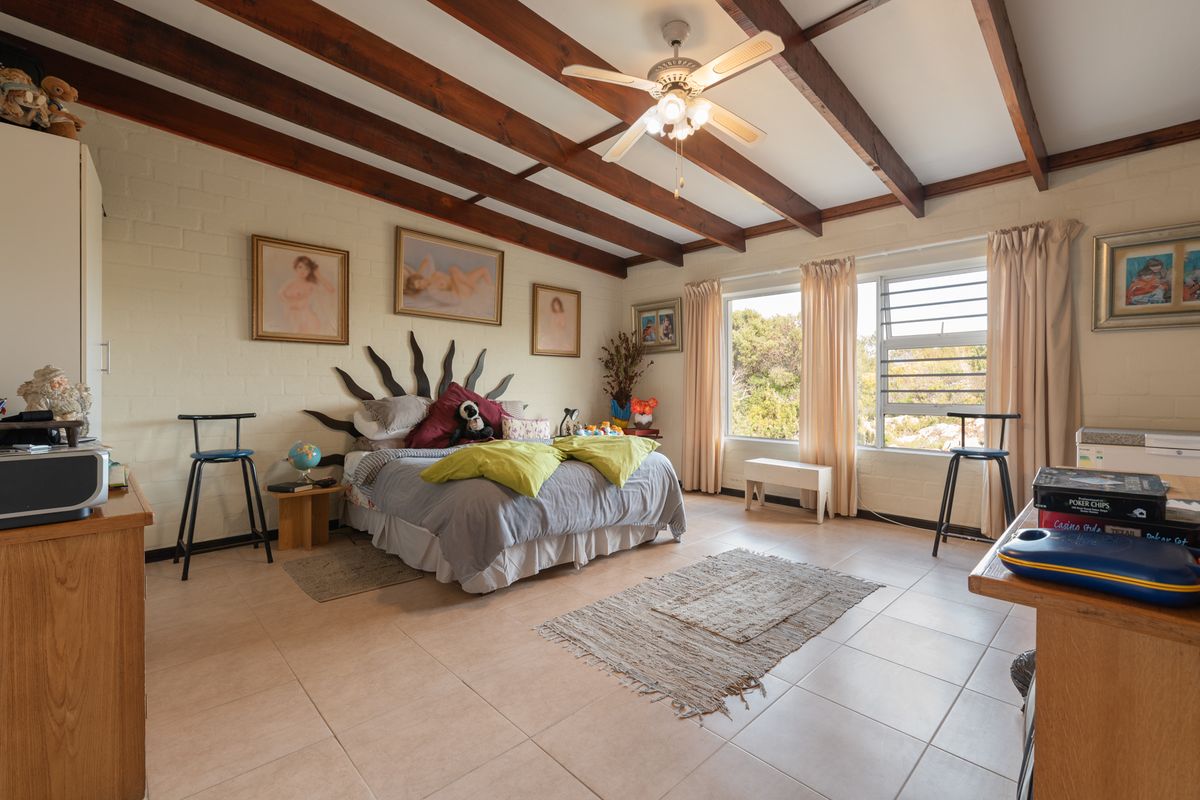 Spacious bedroom featuring exposed timber ceiling beams, a ceiling fan, and large windows providing natural light and garden views.