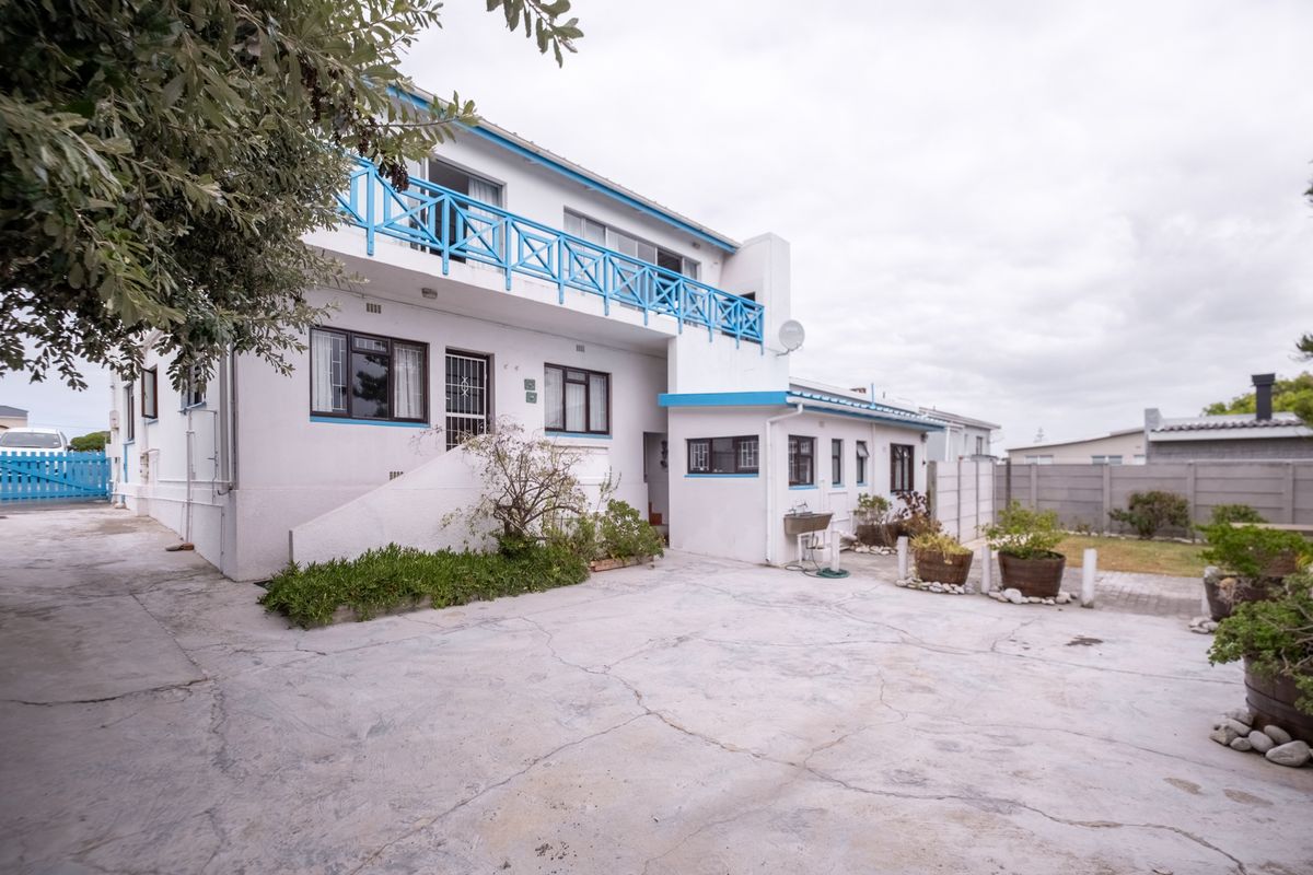 Rear view of a two-story house featuring a paved courtyard, a first-floor balcony with blue railings, and a functional outdoor utility sink.