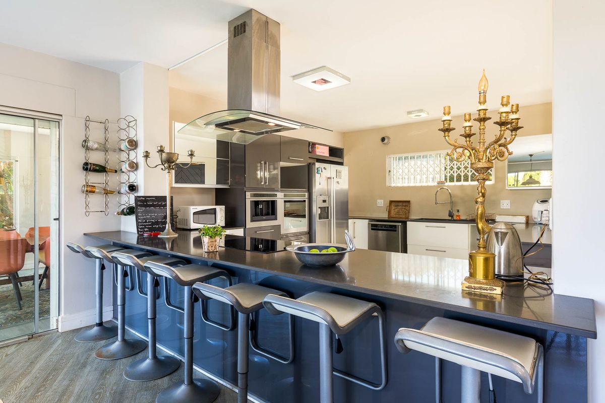 Modern open-plan kitchen featuring a large island with breakfast bar seating, high-end built-in appliances, sleek cabinetry, and stone countertops.