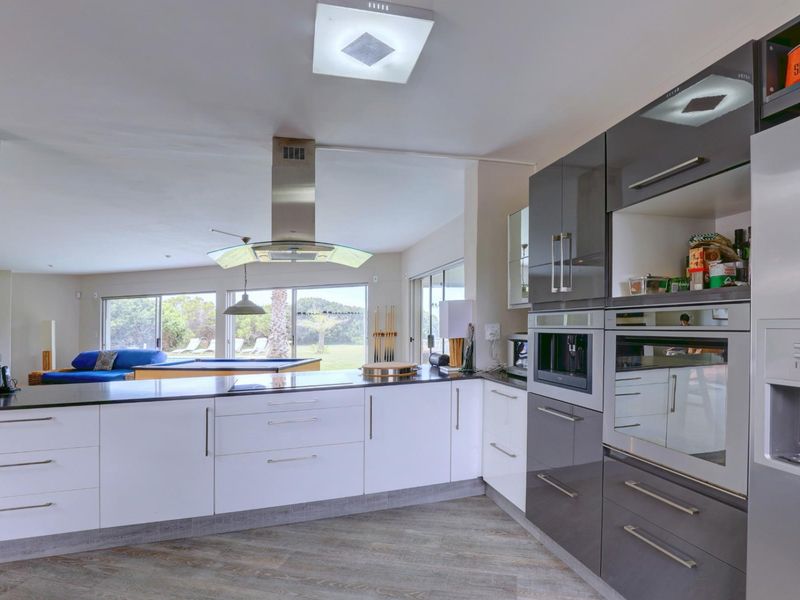Modern open-plan kitchen featuring high-gloss cabinetry, integrated appliances, and stone countertops, seamlessly flowing into the adjacent living area with large sliding glass doors.
