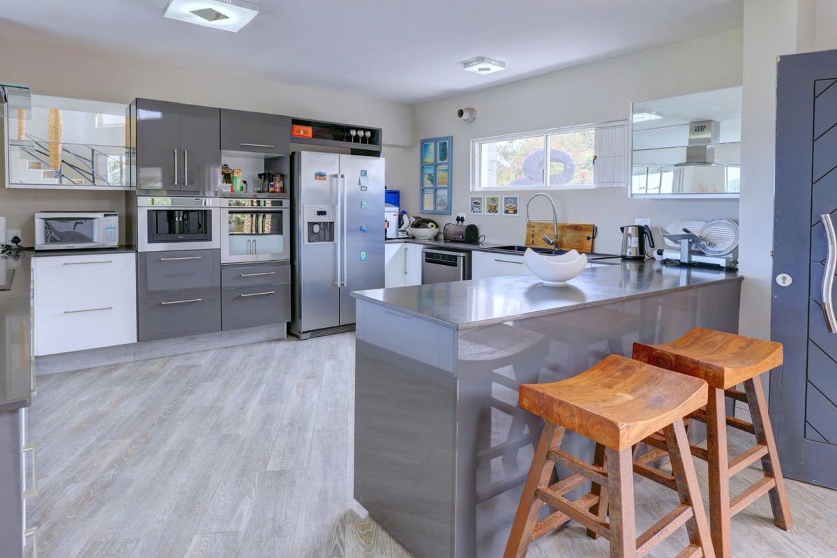 Modern kitchen featuring high-gloss grey cabinetry, a central island with breakfast bar, integrated appliances, and light-toned laminate flooring.