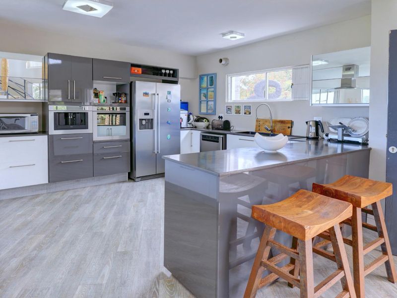 Modern kitchen featuring high-gloss grey cabinetry, a central island with breakfast bar, integrated appliances, and light-toned laminate flooring.