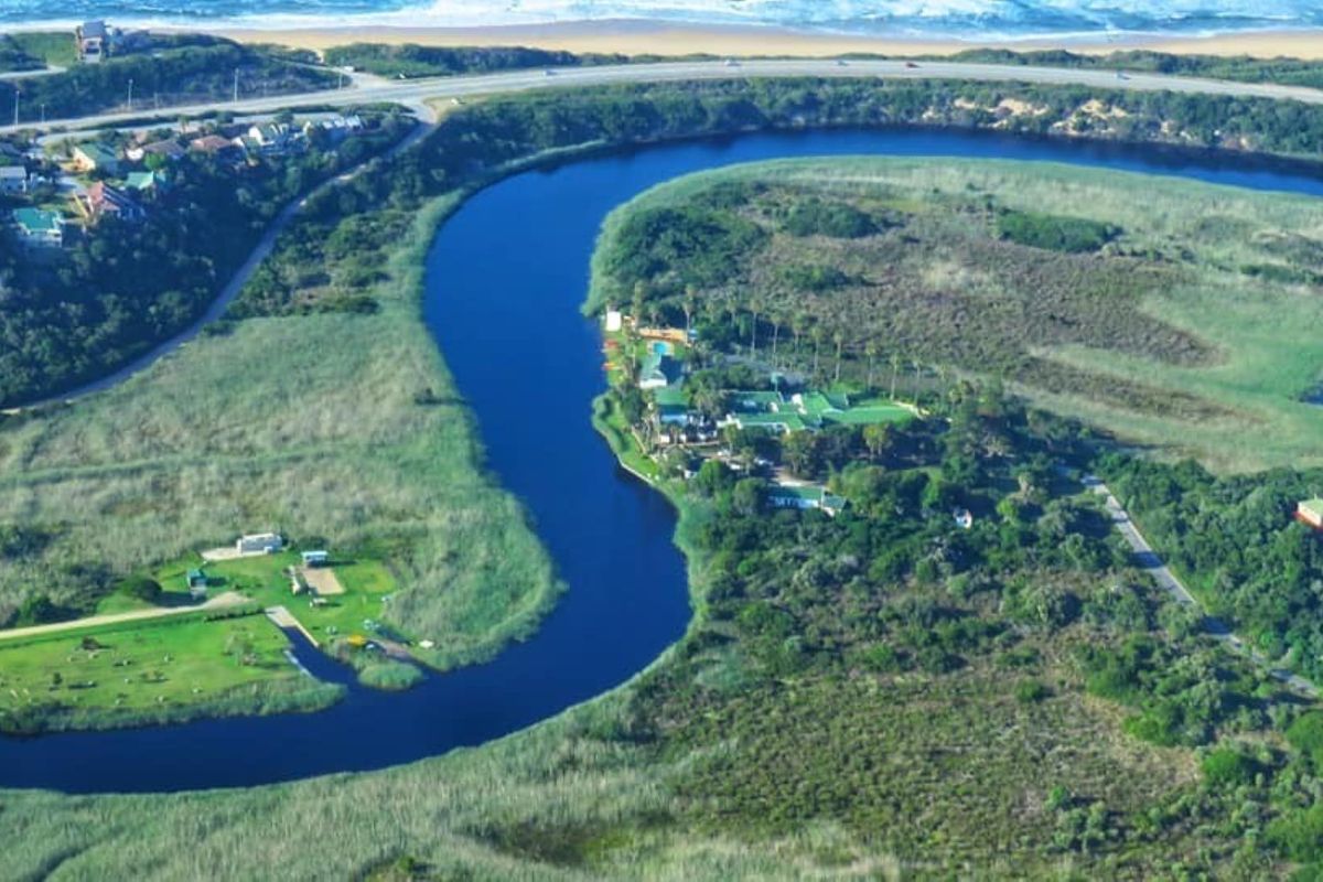An aerial view of the property situated along a winding river, showcasing its scenic coastal location and surrounding natural landscape.