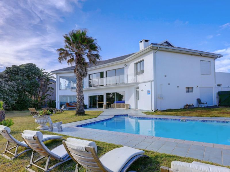 Rear view of a two-story house featuring a swimming pool, landscaped garden, and an upper-level balcony with glass balustrades.