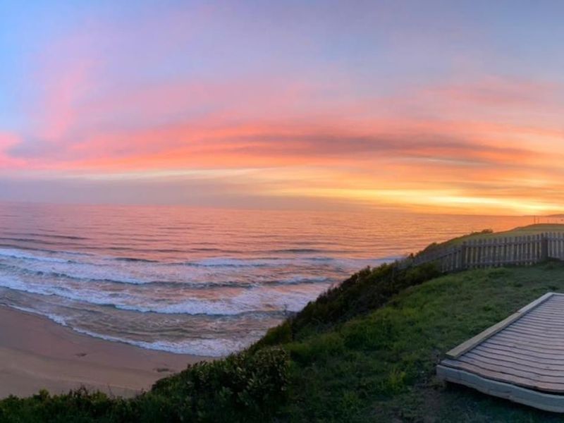 Panoramic ocean view from a coastal property featuring a timber deck and sunset horizon.