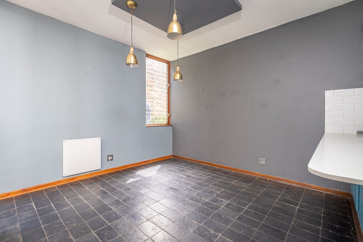 A compact kitchen area featuring dark tiled flooring, contrasting grey walls, pendant lighting, and a white tiled splashback section.