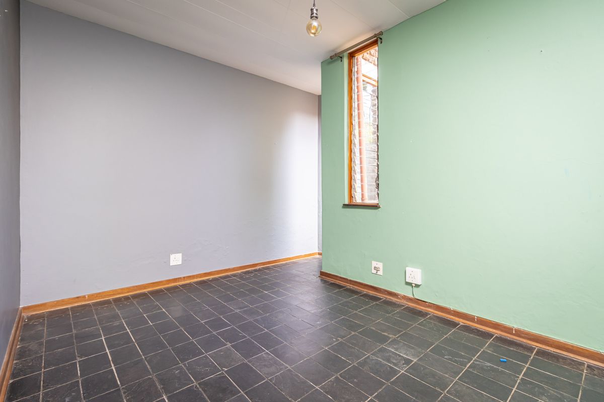 An empty bedroom featuring dark slate-style floor tiles, dual-tone painted walls, and a vertical window with louvre shutters.