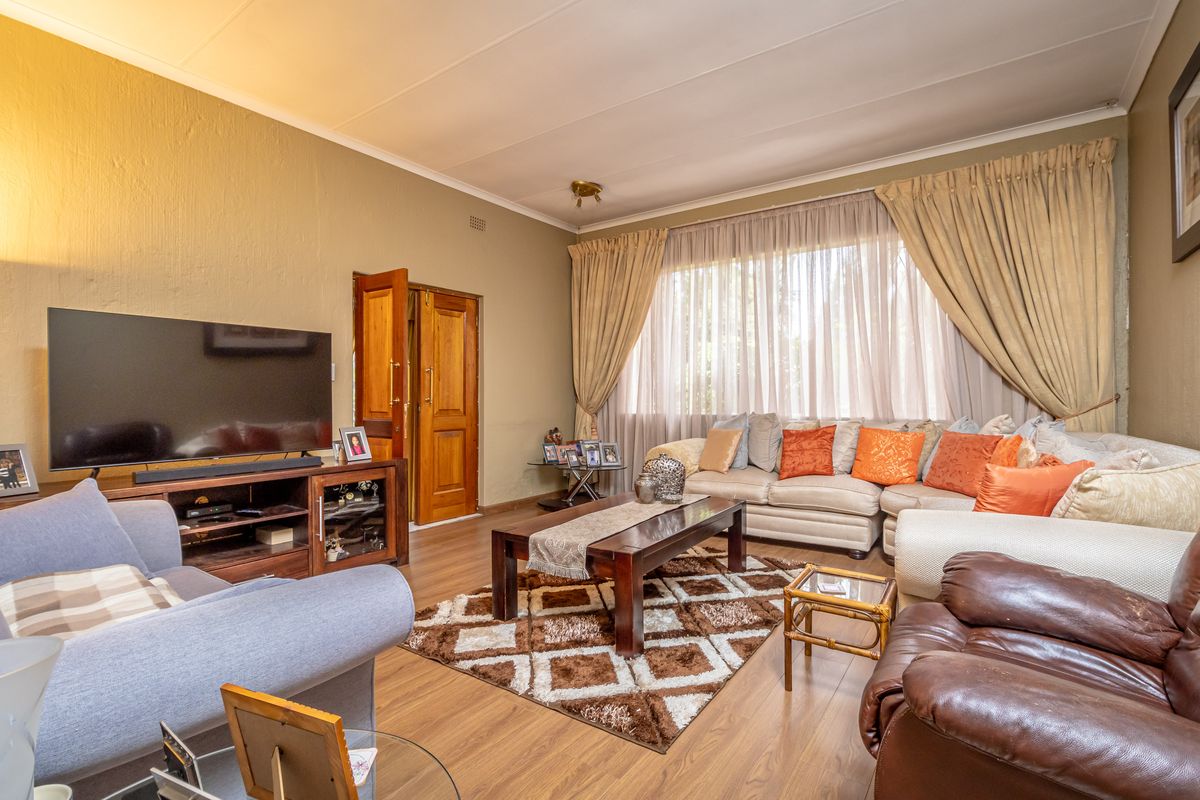 A comfortable living room featuring wood-look flooring, neutral wall tones, and large windows with floor-to-ceiling curtains, providing a warm and inviting atmosphere.