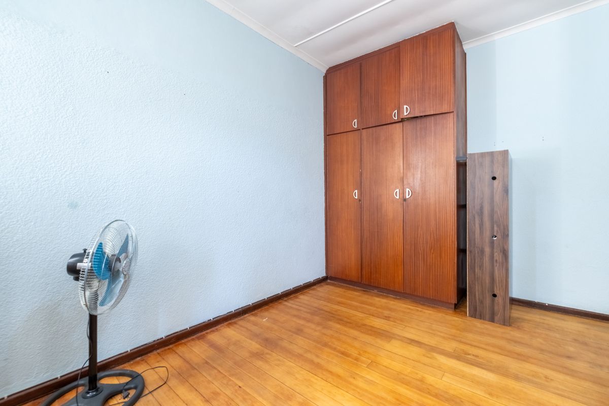 A bedroom featuring hardwood flooring and a large built-in wooden wardrobe with overhead storage compartments.