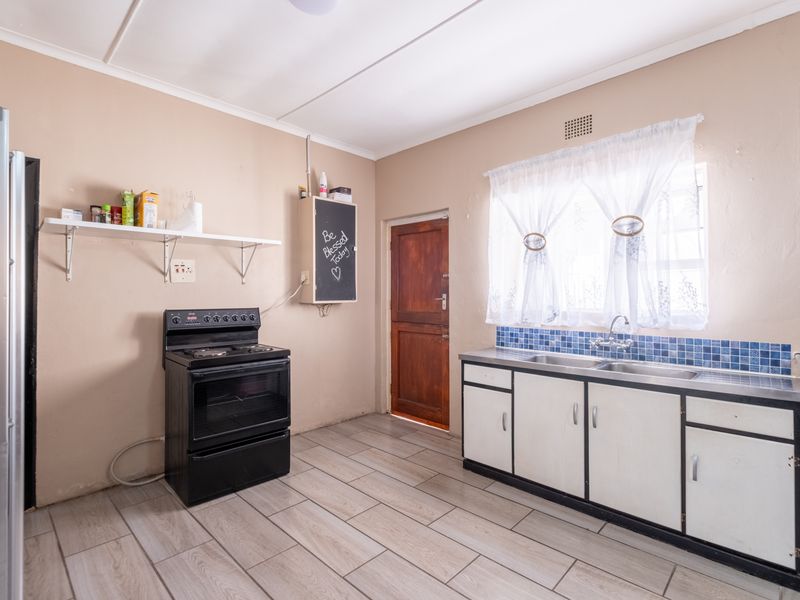 Functional kitchen featuring tiled flooring, a double sink with tiled backsplash, and a freestanding stove, offering potential for cosmetic updates.