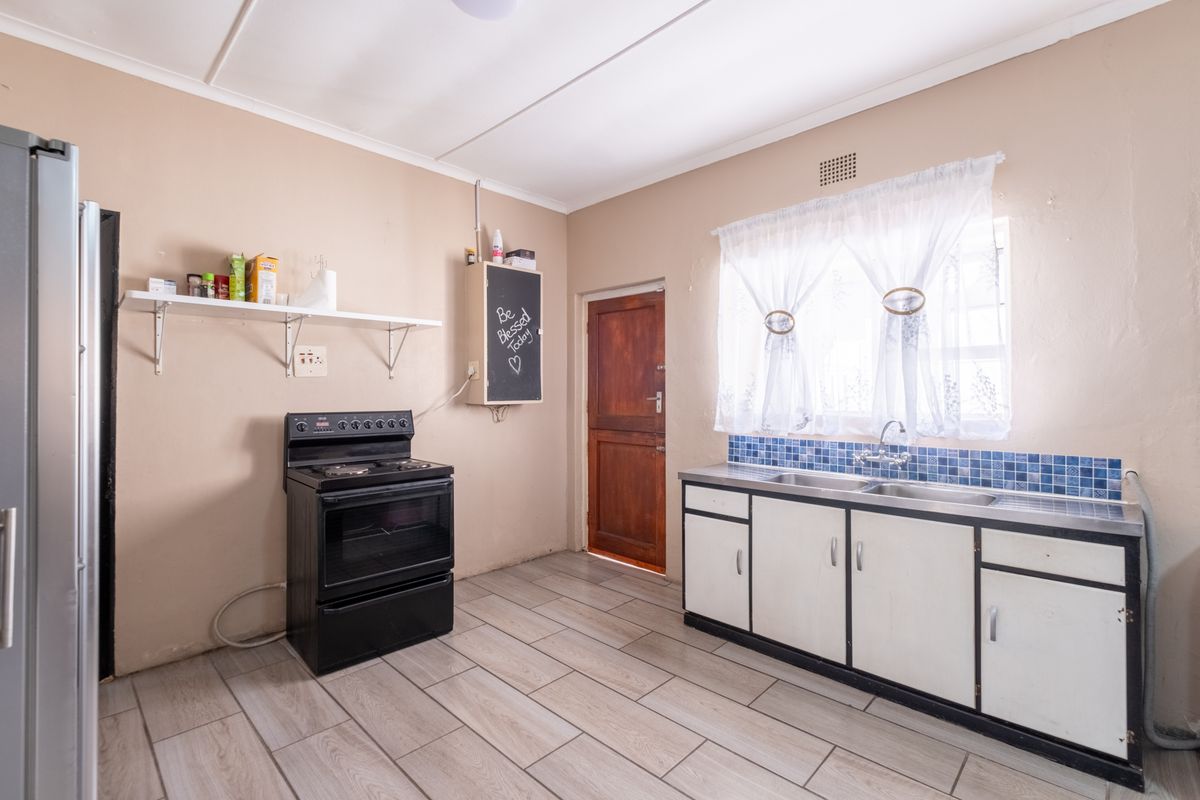 Functional kitchen featuring tiled flooring, a double sink with tiled backsplash, and a freestanding stove, offering potential for cosmetic updates.