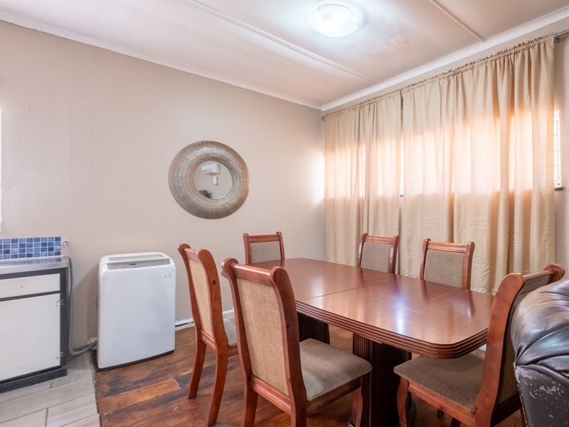 A dining area featuring built-in cabinetry with a tiled splashback, neutral wall tones, and large windows with curtains.