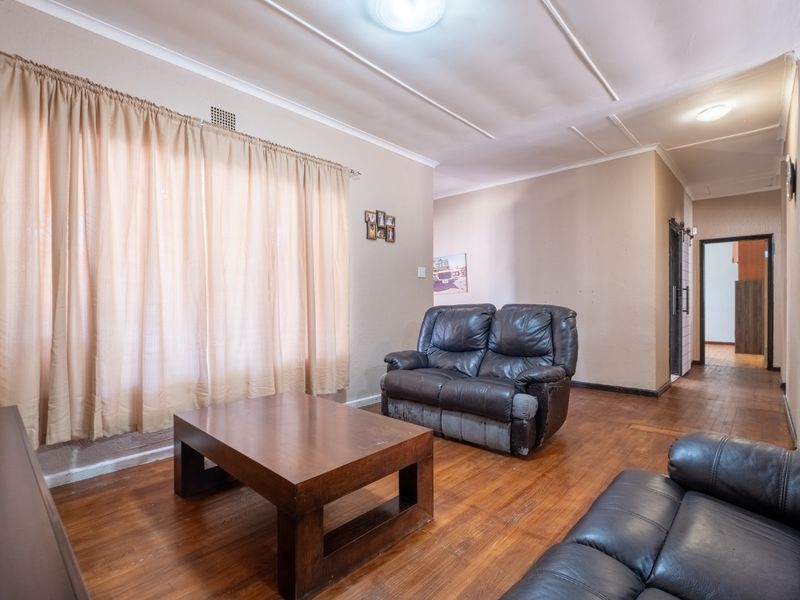 A living room featuring wooden flooring, ceiling molding, and natural light through a large window, offering a functional space with potential for cosmetic updates.
