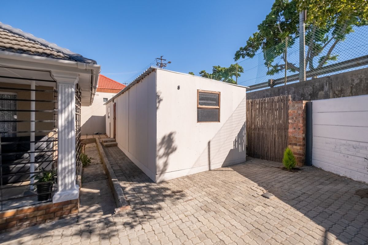 Rear exterior view showing a paved area, boundary wall, and a detached prefabricated structure.