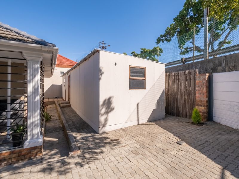 Rear exterior view showing a paved area, boundary wall, and a detached prefabricated structure.