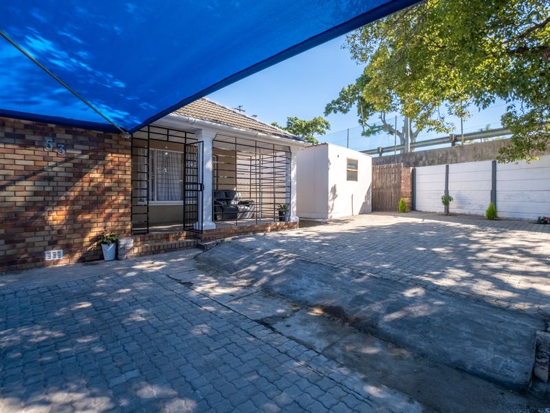 Front exterior view featuring a brick facade, paved driveway, security gate, and a blue shade sail covering the entrance area.