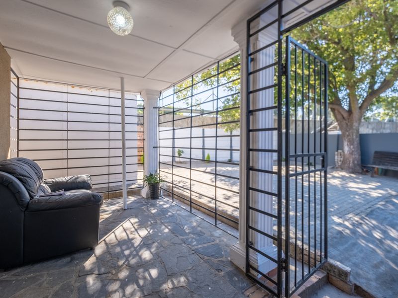 A covered patio area featuring stone flooring, decorative columns, and secure metal security gates, providing a transition space to the outdoor garden area.