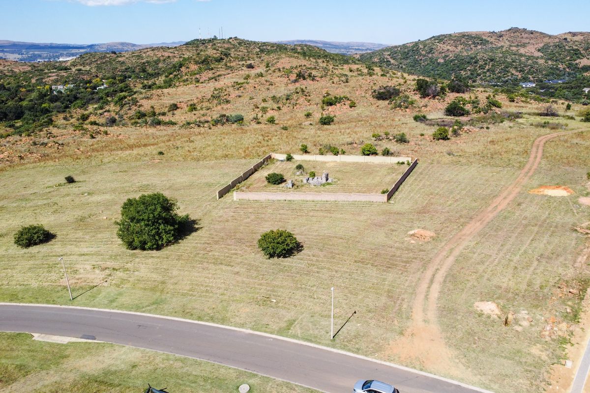 Aerial view of a vacant residential plot featuring a partially walled perimeter, natural landscape, and access to a paved road.