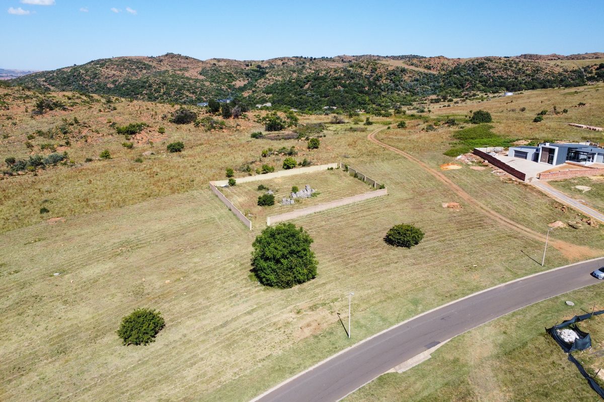 Aerial view of a vacant residential plot featuring a walled perimeter, natural landscape, and surrounding hilly terrain in a developing estate.