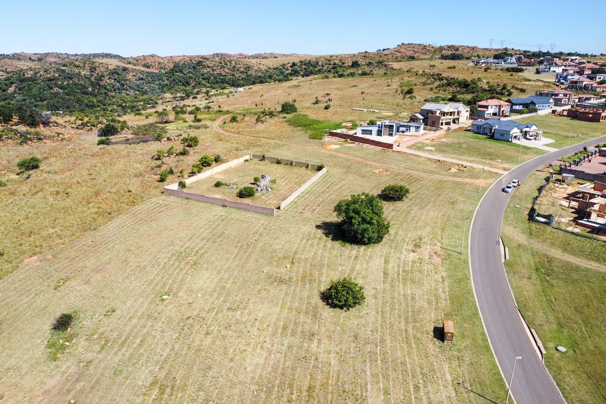 Aerial view of a vacant residential plot in a developing estate, featuring established boundary walls and surrounding natural landscape.