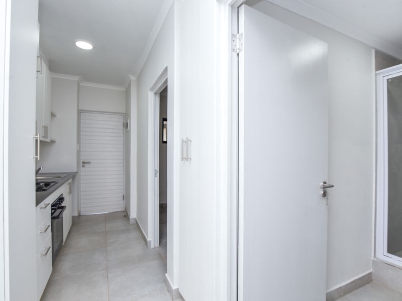 A modern, clean apartment interior featuring a compact kitchen area with built-in cabinetry and a separate bathroom with a glass-enclosed shower.