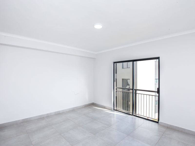 A bright, empty bedroom featuring neutral floor tiles, white walls, and a sliding glass door providing access to a private balcony.
