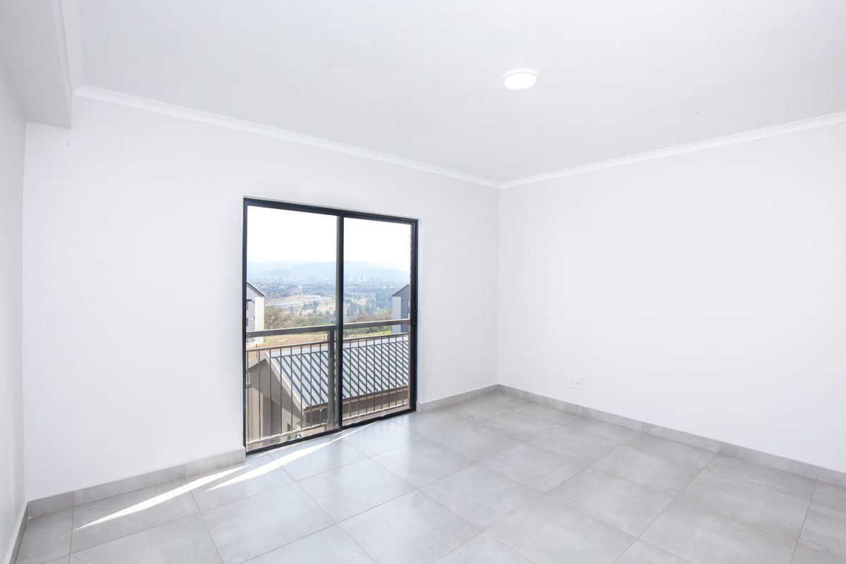 A bright, empty bedroom featuring neutral floor tiles, white walls, and a sliding glass door leading to a balcony with scenic views.