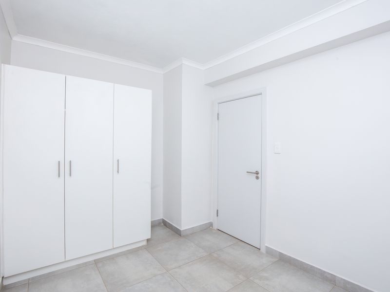 A clean, minimalist bedroom featuring neutral floor tiles and built-in white cabinetry, offering a bright and versatile living space.